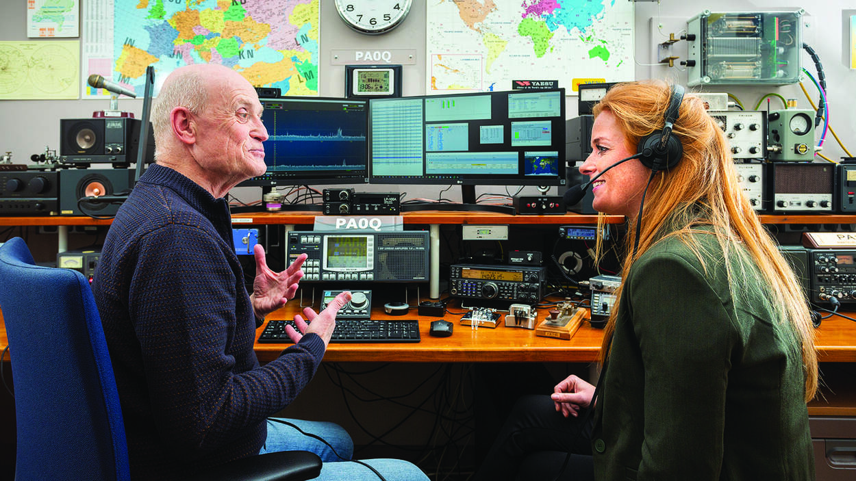Vrouw met koptelefoon op in gesprek met een radiozendamateur bij apparatuur