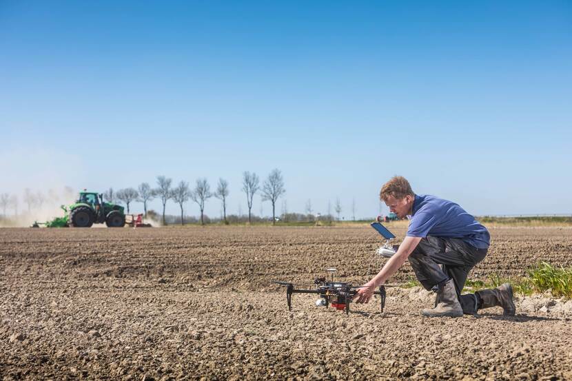 Knielende man met drone op een landbouwgrond met tractor op de achtergrond