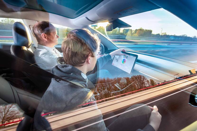 Man en kind in elektrische auto Tesla, rijdend terwijl kind tablet bedient