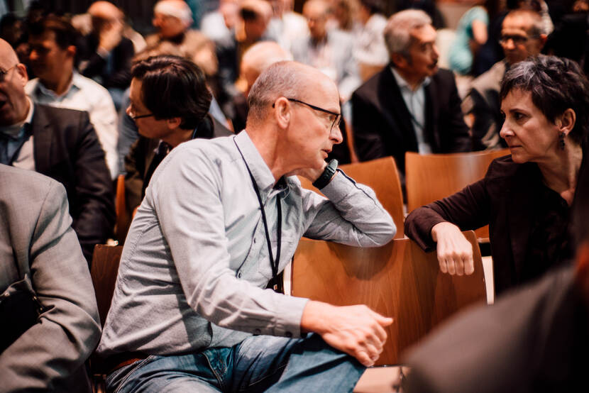 Een man en vrouw tijdens in een zaal op stoelen tijdens symposium opstap naar weerbaarheid in 2019