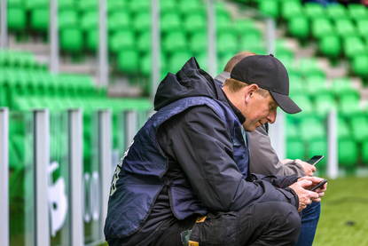 Bezoekers aan een voetbalwedstrijd kijken op hun smartphone