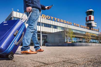 Man met koffer en telefoon in zijn hand voor Rotterdam Airport