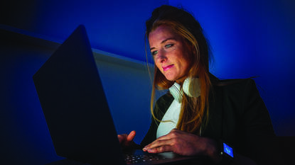 Vrouw in donkere kamer achter laptop met koptelefoon om haar nek