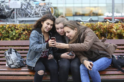 Drie tienermeiden die naar 1 smartphone kijken buiten